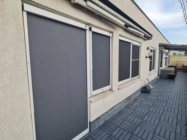 Een verticaal zonnescherm aan de buitenkant van diverse ramen en een terrasdeur beschermt de gevel van het huis tegen zon en hitte.